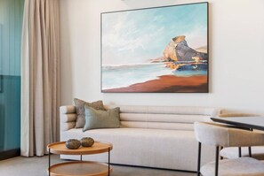 A modern living room with a sofa, a coffee table, and a painting of a coastal landscape.