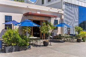 An outdoor seating area with tables and chairs, blue umbrellas, and potted plants.
