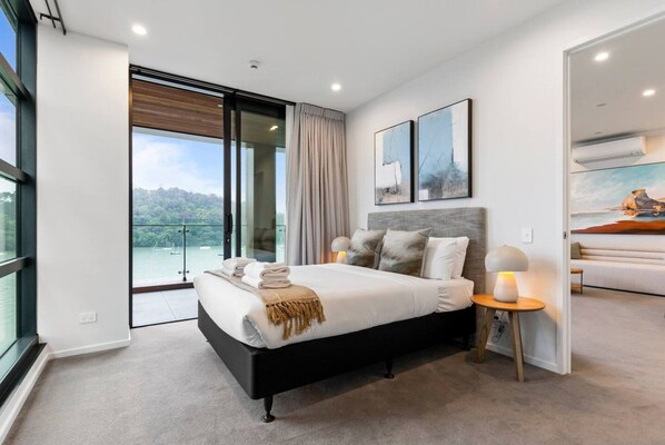 A modern bedroom with a large bed, a nightstand, and a view of a balcony.