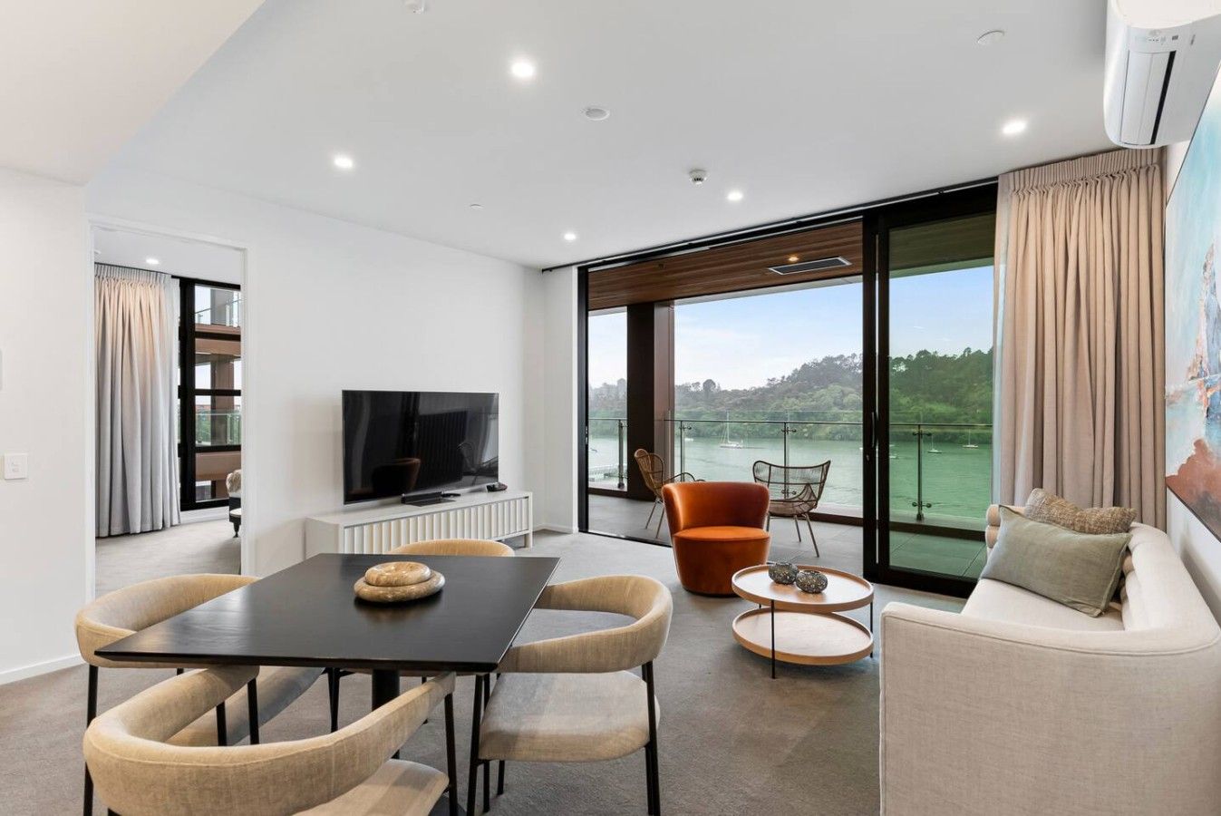 A modern living room with a flat-screen TV, a dining table, and a sofa.