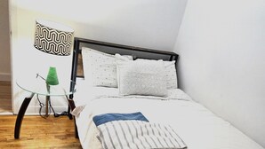 A neatly made bed with white bedding and a striped pillow, a glass table with a green object on it, and a wooden floor.
