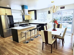 A modern kitchen with a central island, stainless steel appliances, and a dining area with bar stools. - Charming home in Sainte-Foy with high-end amenities—the perfect turnkey solution! (Québec)