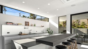 Een moderne keuken met een centraal eiland, barkrukken en een groot raam met uitzicht op een bergachtig landschap.