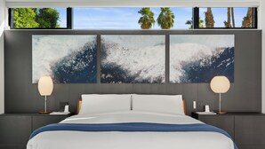 Een moderne slaapkamer met een groot bed, twee nachtkastjes en drie kunstwerken aan de muur, die golven in de oceaan afbeelden.