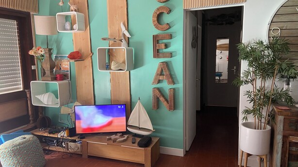 A living room with a teal accent wall, wooden letters spelling "OCEAN", a television, and various decorative items.