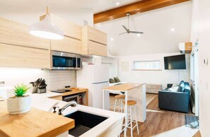 A modern kitchen with wooden cabinets, a microwave, and a sink. There is a dining area with a table and chairs, and a TV mounted on the wall. - Boutique Riverside Loft Near Downtown (Calgary)