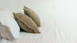 Quarto com cama, duas almofadas, um quadro na parede e uma janela.