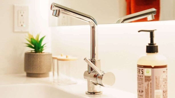 A bathroom with a white sink, chrome faucet, and a bottle of soap. - Boutique Riverside Loft Near Downtown (Calgary)