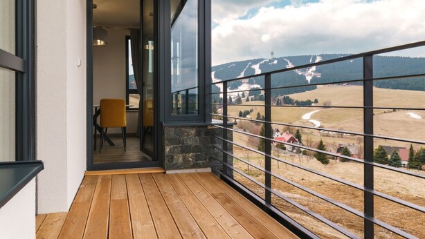 Ein Balkon mit Holzboden und einer Glastür, die zu einem Innenraum führt.