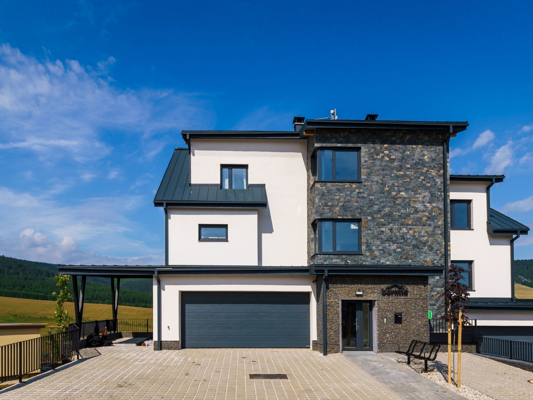 Une maison moderne à deux étages, dotée d’un garage, d’un patio couvert et d’une façade en pierre.