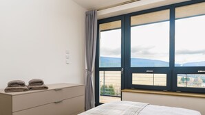 Ein Schlafzimmer mit Bett, Schminktisch und einem Fenster mit Blick auf die Landschaft.