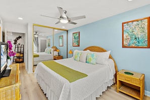 A bedroom with a bed, bedside tables, a mirror, and a ceiling fan. - Modern Comfort with Breathtaking Ocean Views (Kihei)