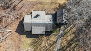 Ein rechteckiges Gebäude mit flachem Dach und Schornstein, umgeben von trockenem Gras und vereinzelten Bäumen.