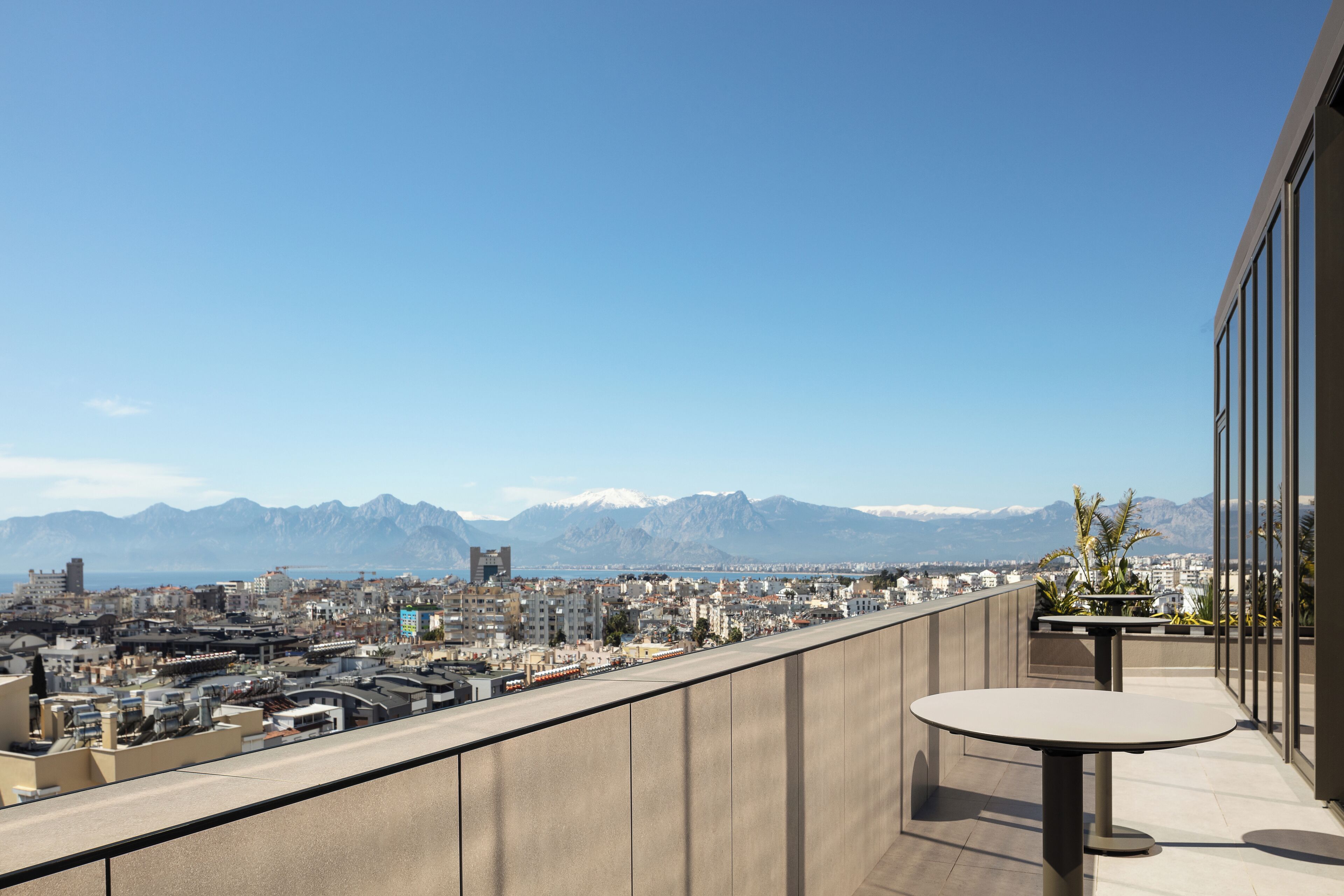 Un balcón con una mesa y sillas, con vistas a un paisaje urbano y montañas al fondo.