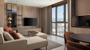 A modern living room with a large flat-screen TV, a sofa, a coffee table, and a dining area with chairs.