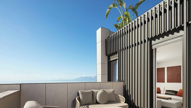 A modern outdoor seating area with a sofa and chairs, a round table, and a view of the ocean.