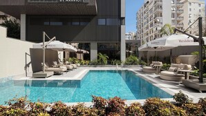 A swimming pool area with lounge chairs and umbrellas, a Marriott Residence Inn building in the background, and a clear blue sky.
