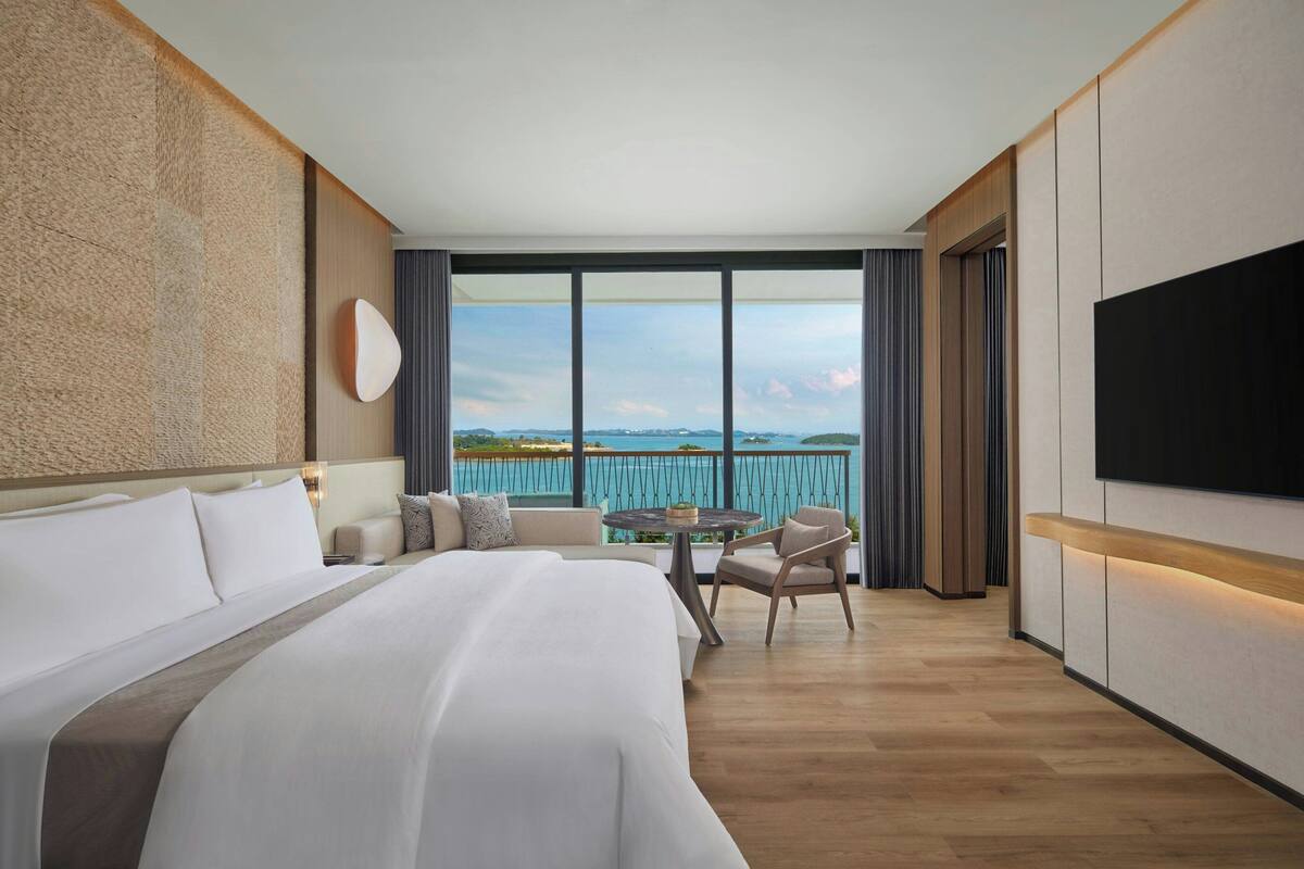 Una habitación de hotel moderna con una cama grande, una mesa redonda y vistas al mar.