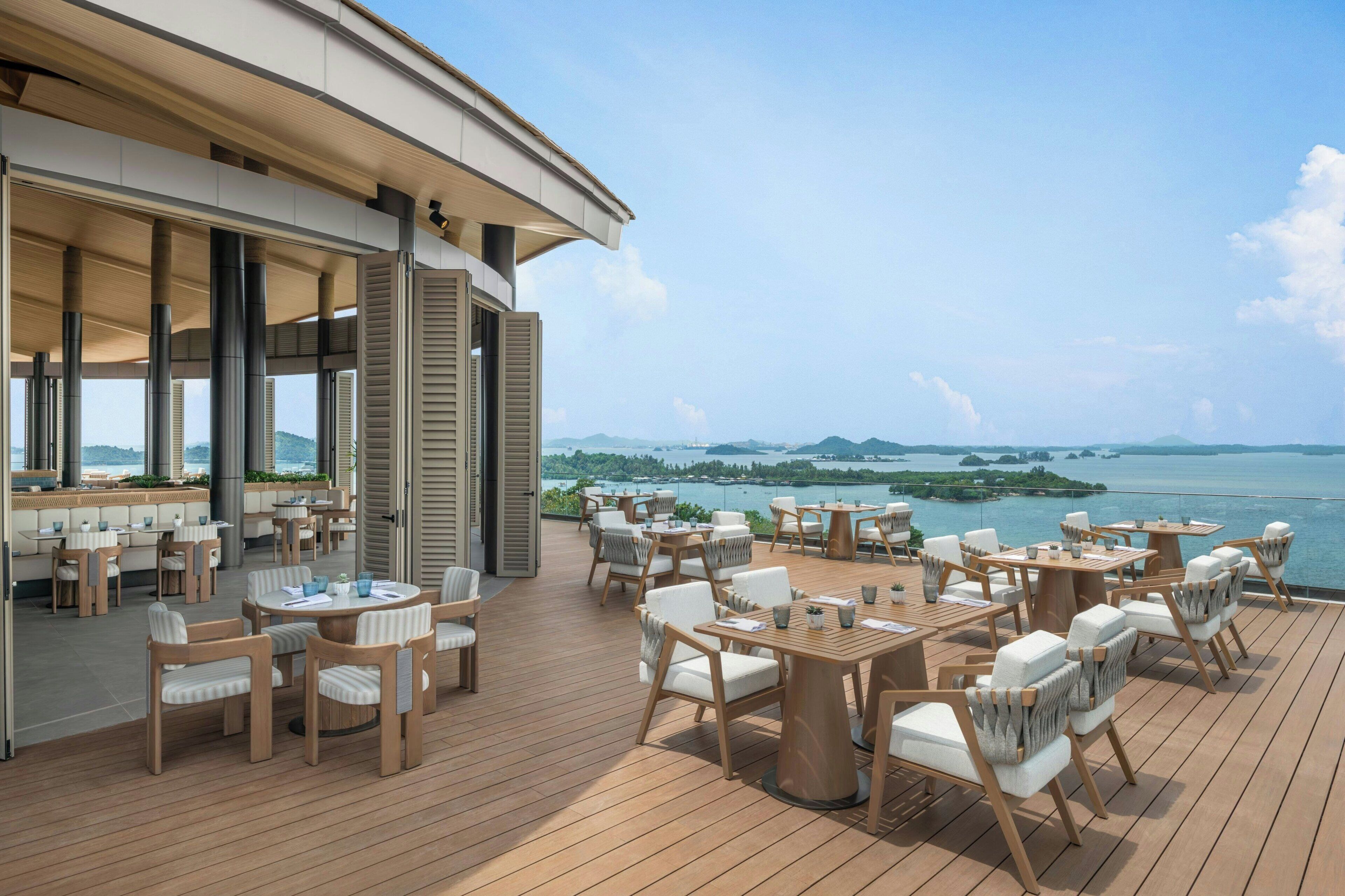 Una terraza con asientos al aire libre, vista al mar y un edificio con grandes ventanales.