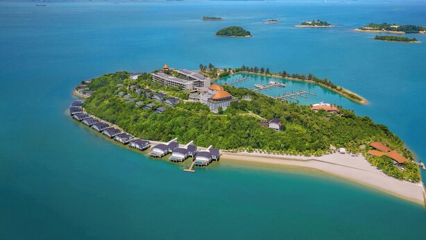 An aerial view of a tropical island resort with a central building surrounded by lush greenery, a marina, and a beach. - The Westin Nirup Island Resort & Spa (Nirup Island)