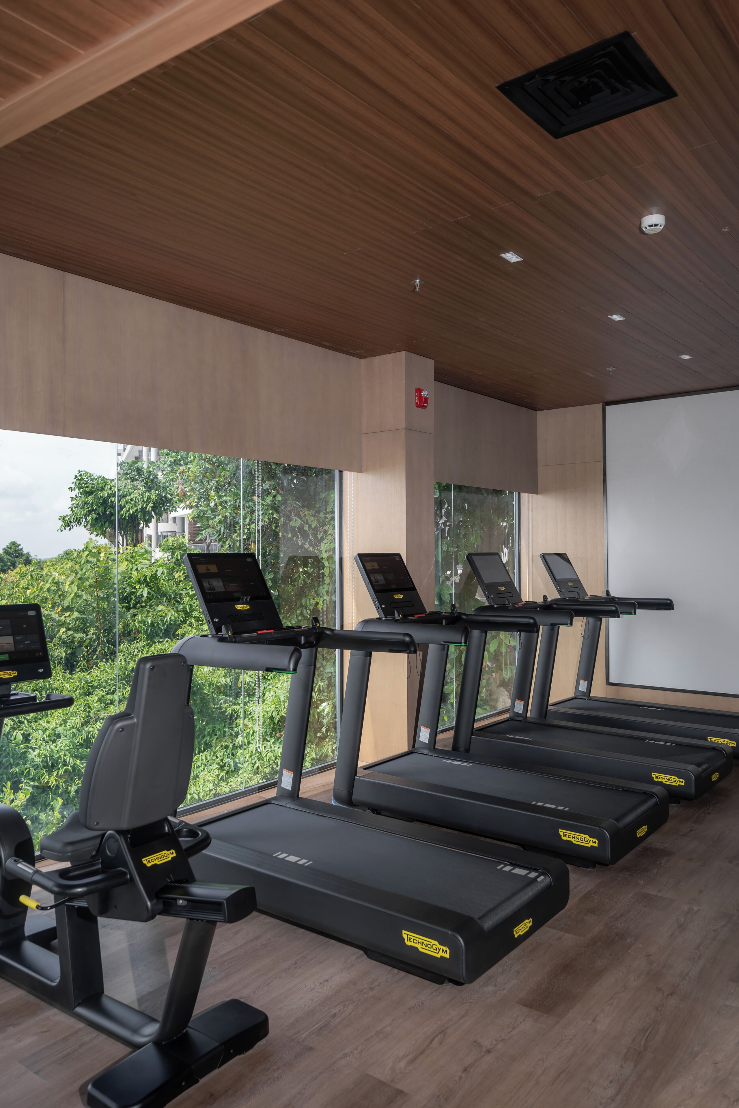 Un gimnasio con cintas de correr, bicicletas estáticas y un amplio ventanal con vistas al verdor.