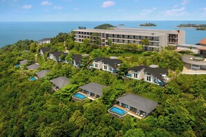 Um resort com vários edifícios cercados por vegetação exuberante, com piscinas e vista para o mar.