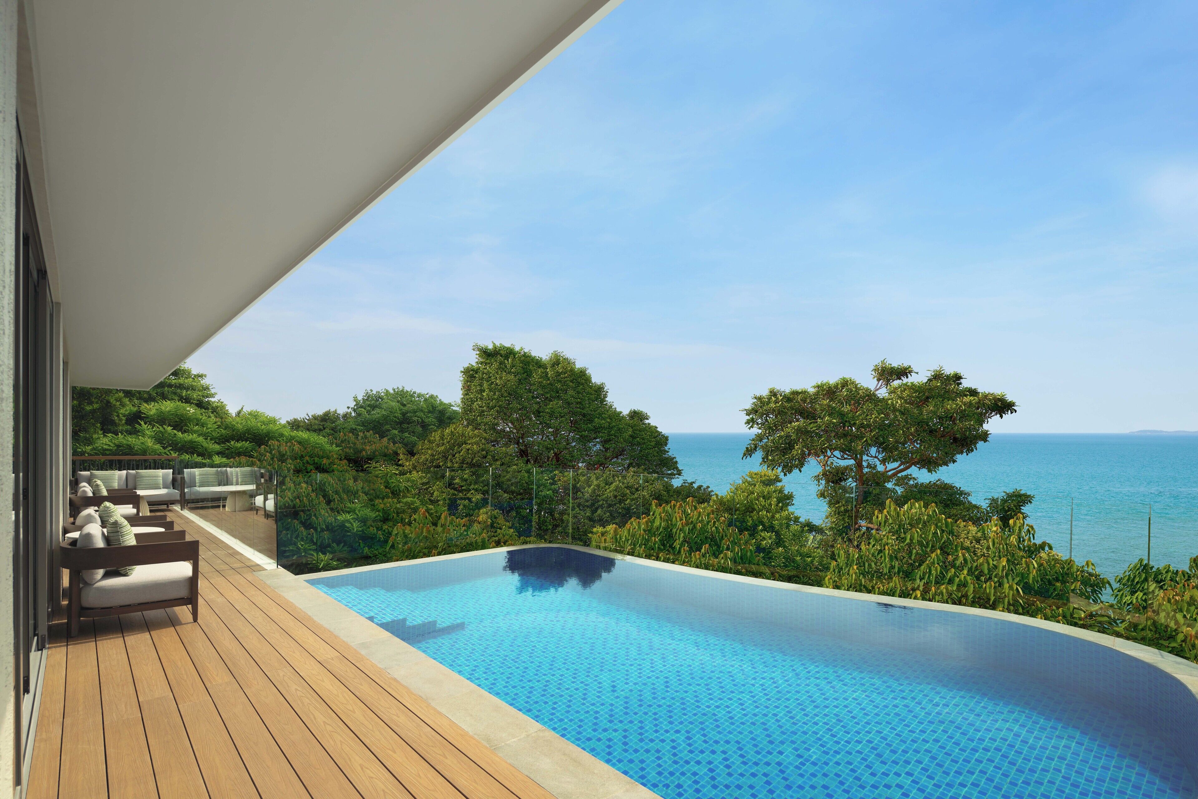 A swimming pool with a wooden deck and outdoor seating, overlooking a body of water and greenery.