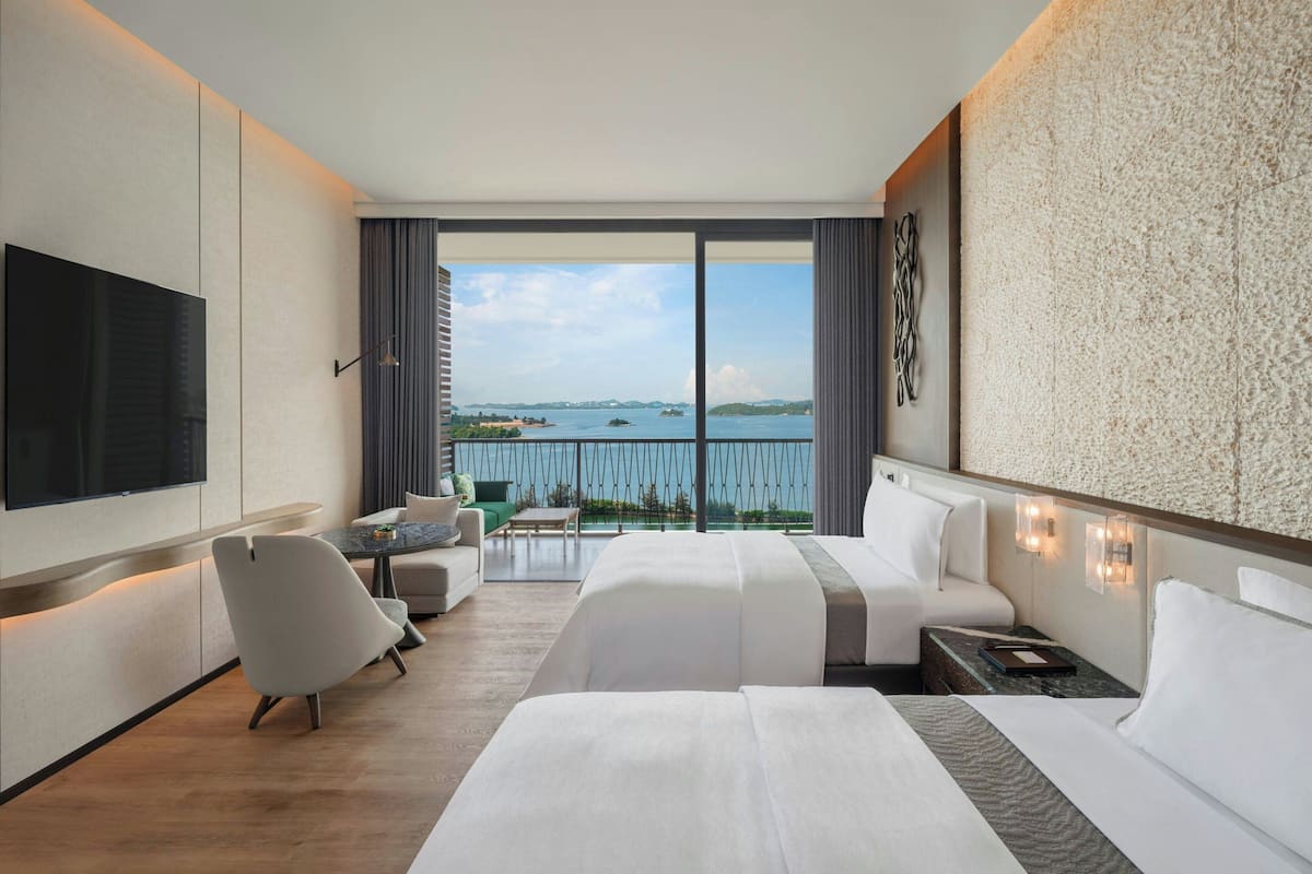 Habitación de hotel con una cama grande, televisión, escritorio y balcón con vista al mar.