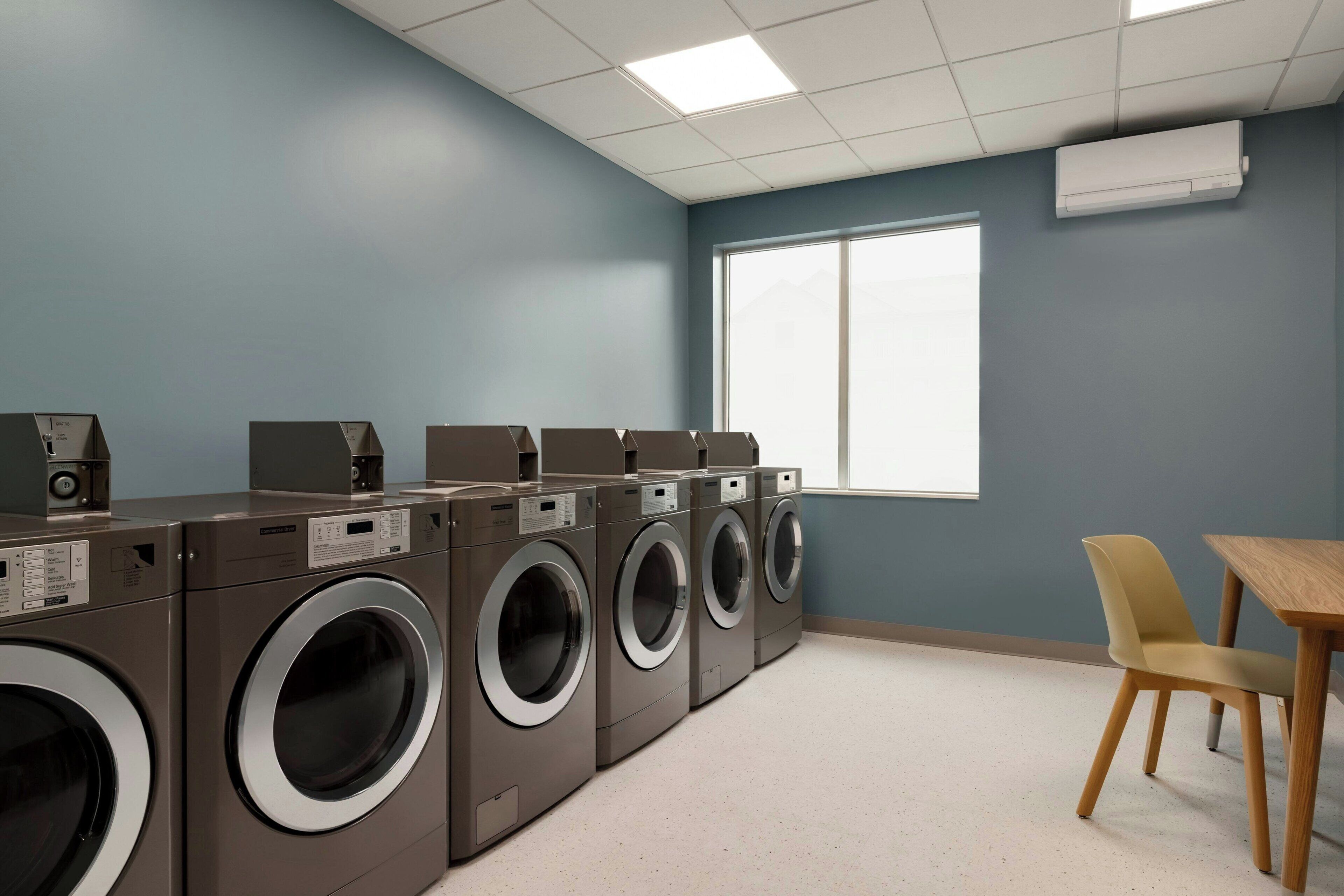 A laundry room with multiple washing machines, a table, and chairs.