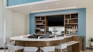 A modern kitchen with a central island, bar stools, and built-in shelves with various bottles and glasses. - Element by Marriott Charleston Airport (North Charleston)