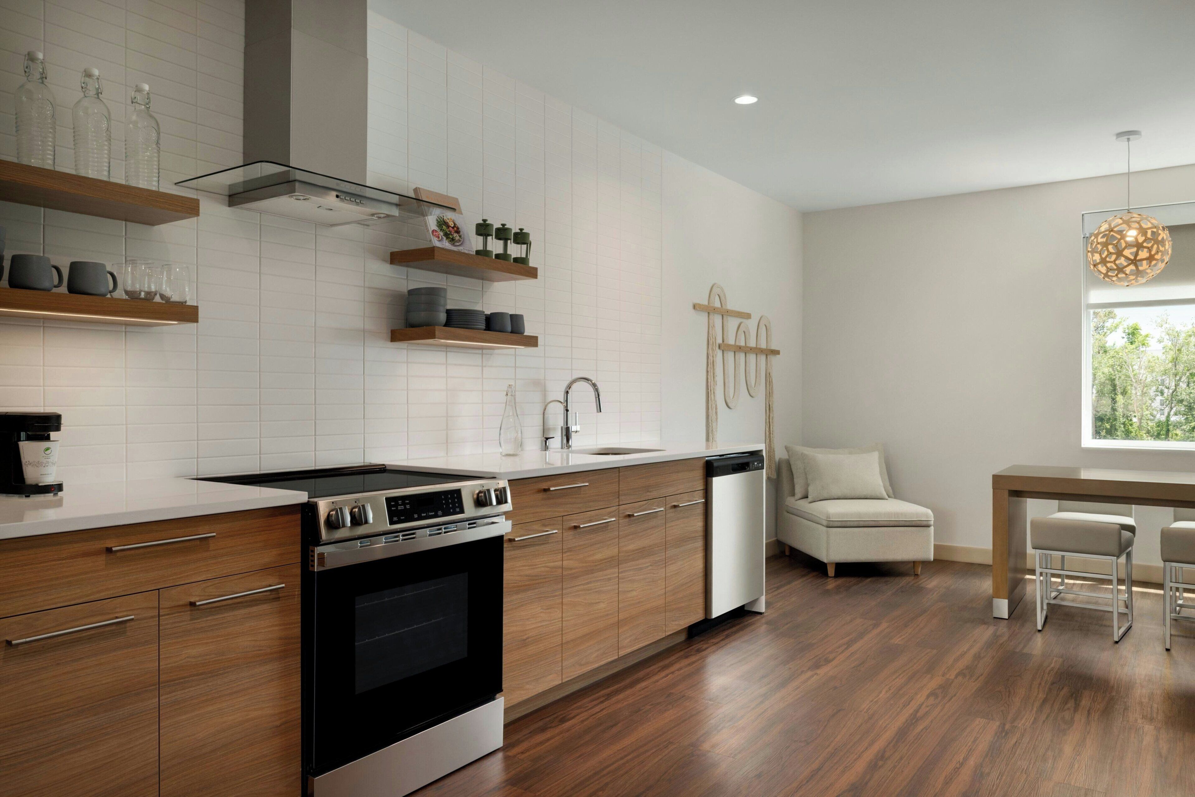 A modern kitchen with wooden cabinets, a built-in oven, and a dishwasher. There is a dining area with a table and chairs.