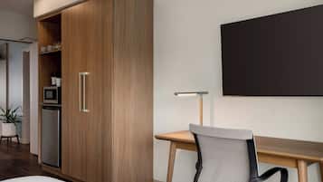 Una habitación de hotel moderna con un armario de madera, un escritorio con silla, un televisor de pantalla plana y una pequeña kitchenette.
