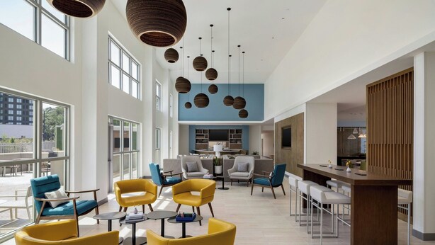 A spacious lounge area with modern yellow chairs, a central coffee table, and a bar area with stools. - Element by Marriott Charleston Airport (North Charleston)