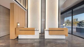 A modern reception area with two wooden reception desks, a vertical light panel, and a large glass window offering a city view. - Fairfield by Marriott Hangzhou Gongshu (Hangzhou)