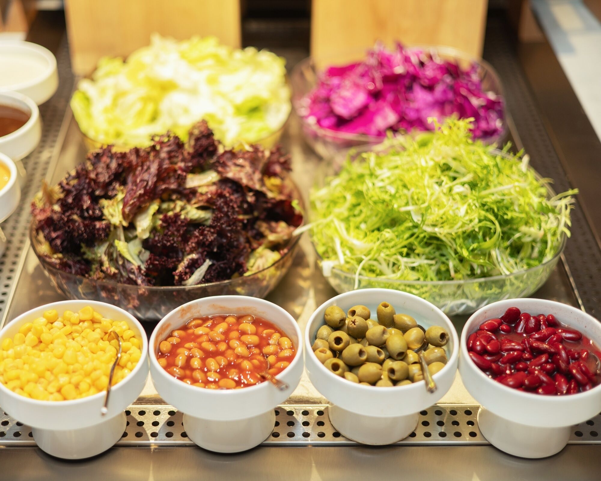 A variety of food items including salads, beans, and olives arranged on a metal tray.