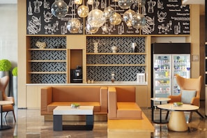 Un espace détente moderne comprenant un canapé, une machine à café et un réfrigérateur rempli de boissons.