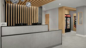 A reception area with a modern design, featuring a reception desk, a refrigerator with snacks, and a wooden slatted wall. - TownePlace Suites by Marriott® Jacksonville Mayport (Atlantic Beach)