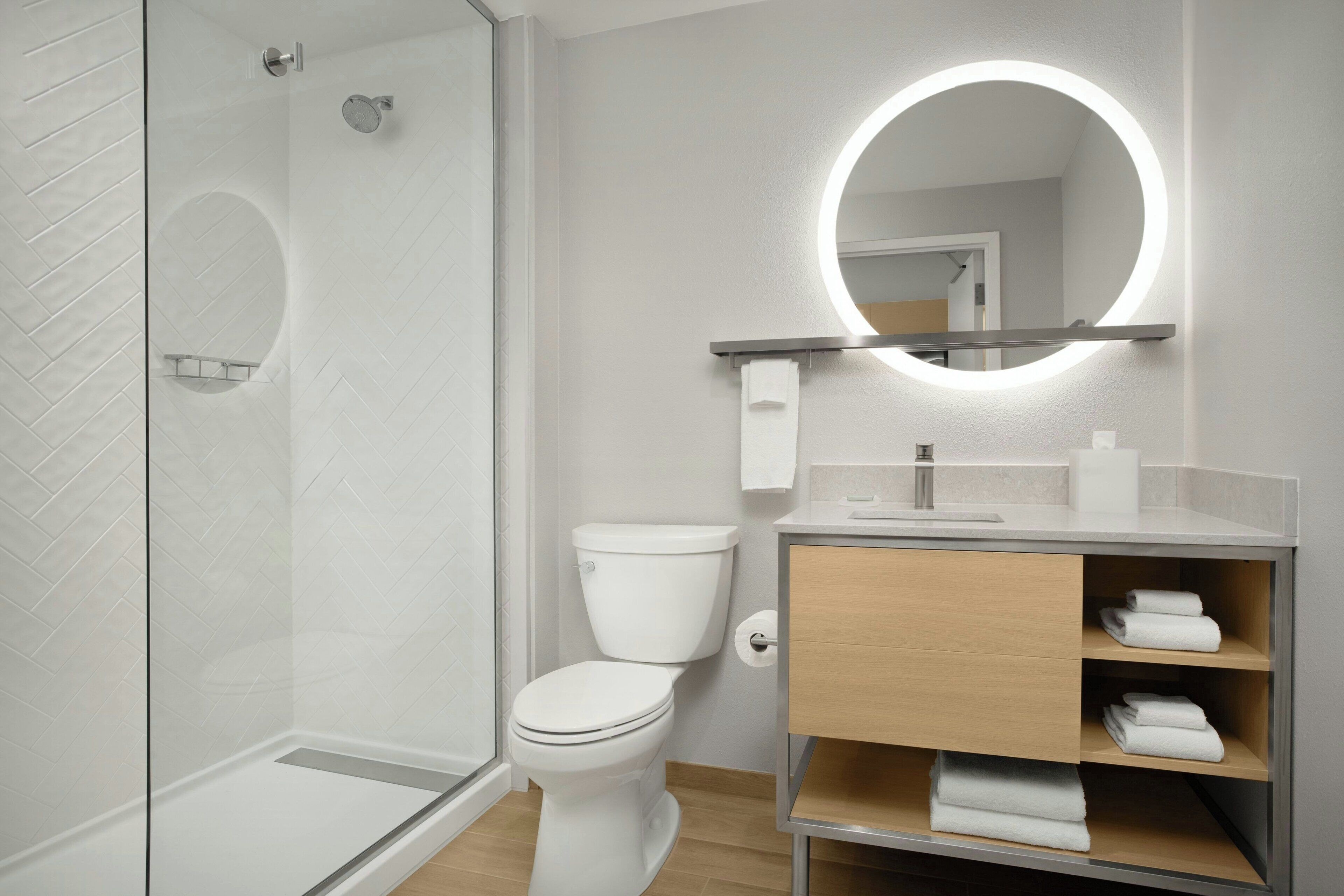 Une salle de bain moderne avec une douche à parois de verre, des toilettes, un meuble-lavabo avec un miroir et des étagères avec des serviettes.