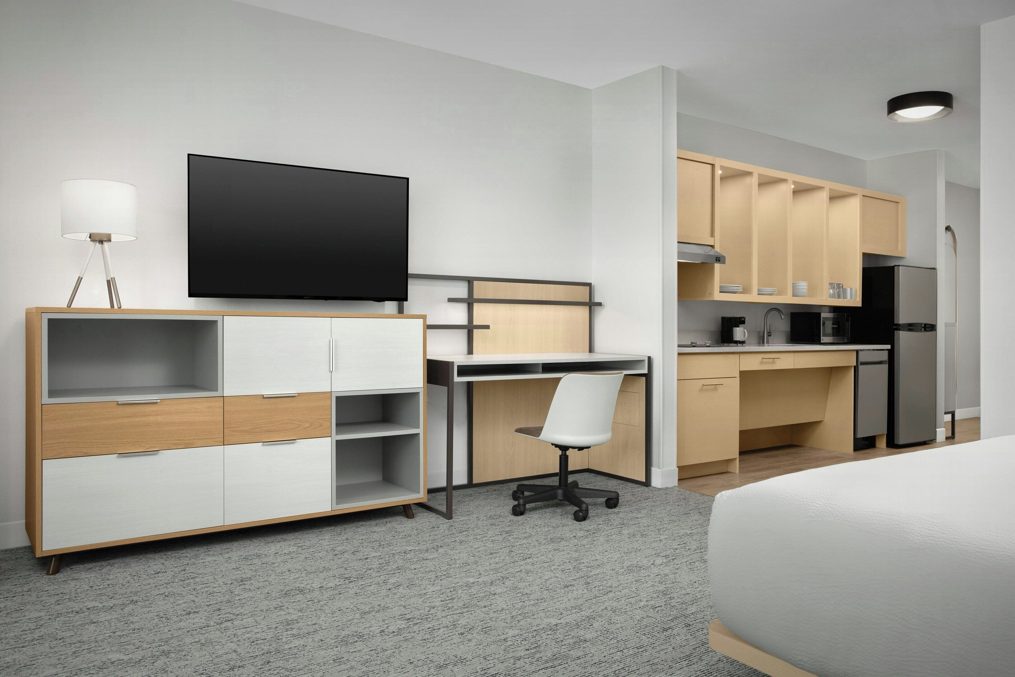 Een moderne hotelkamer met een bed, een bureau, een stoel, een televisie, een kitchenette en een kledingkast.