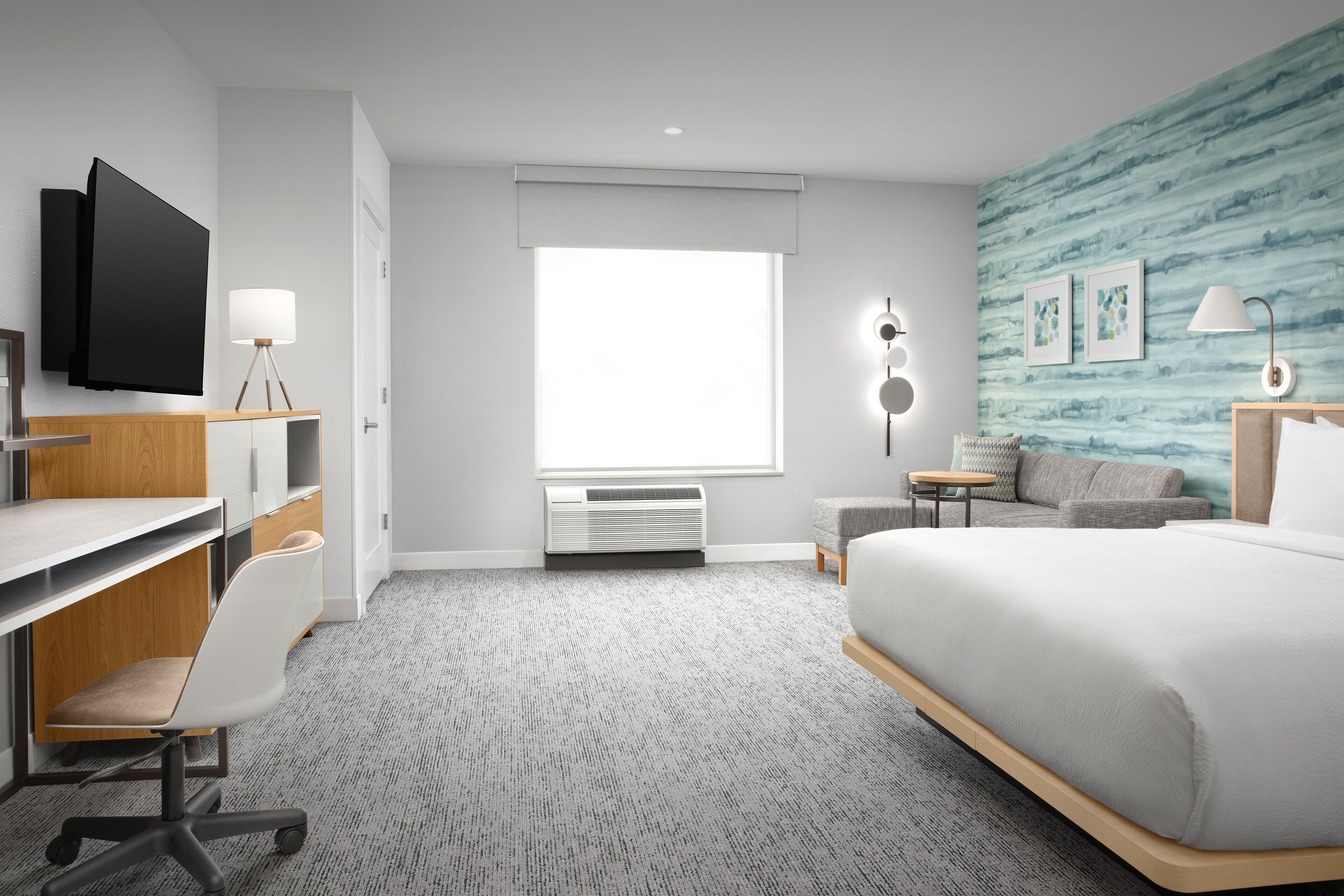 Una habitación de hotel moderna con cama, escritorio, silla, televisor y un ventanal grande.