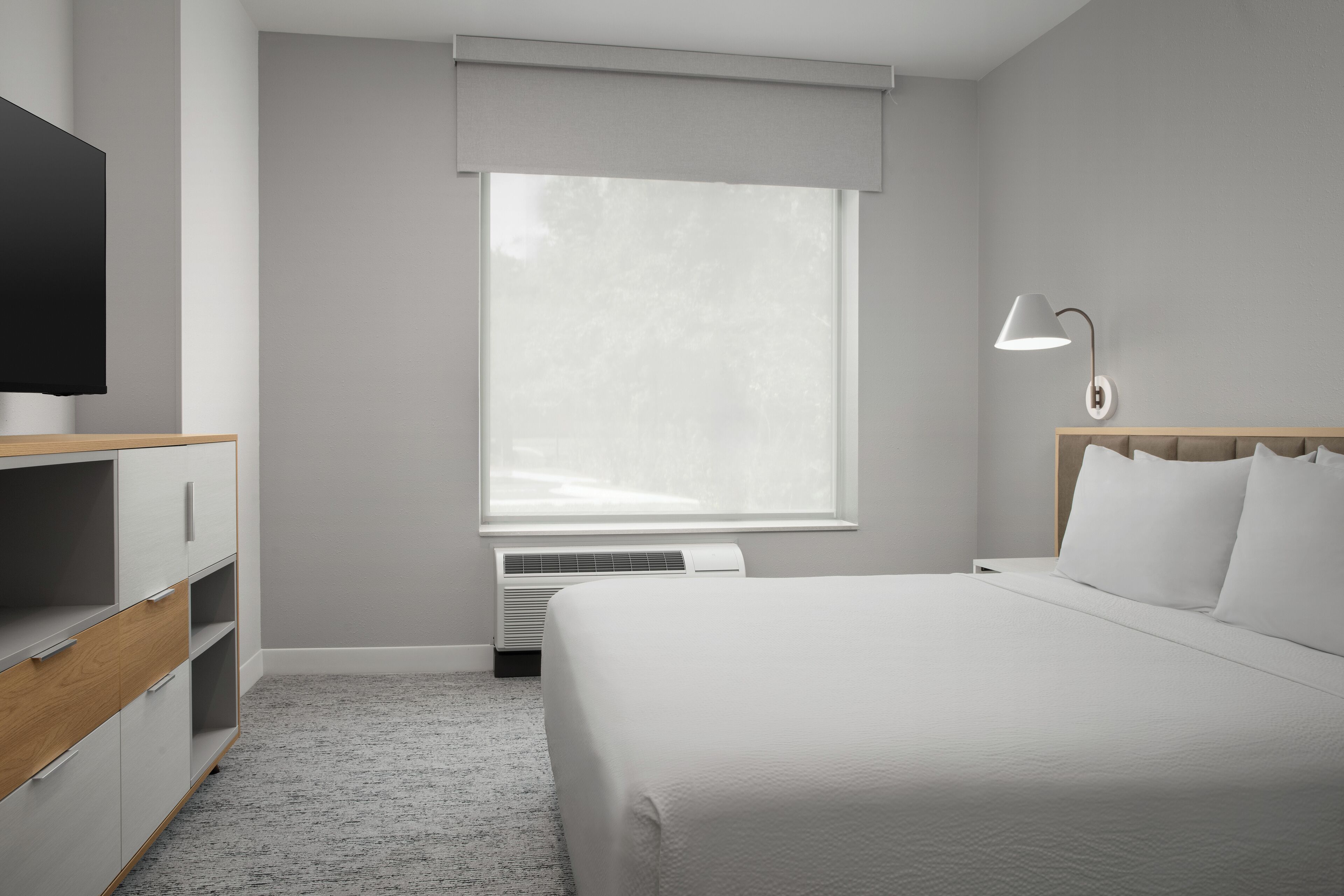 Ein Hotelzimmer mit einem Bett, einem Fernseher, einem Schreibtisch, einer Lampe und einem Fenster mit Jalousien.