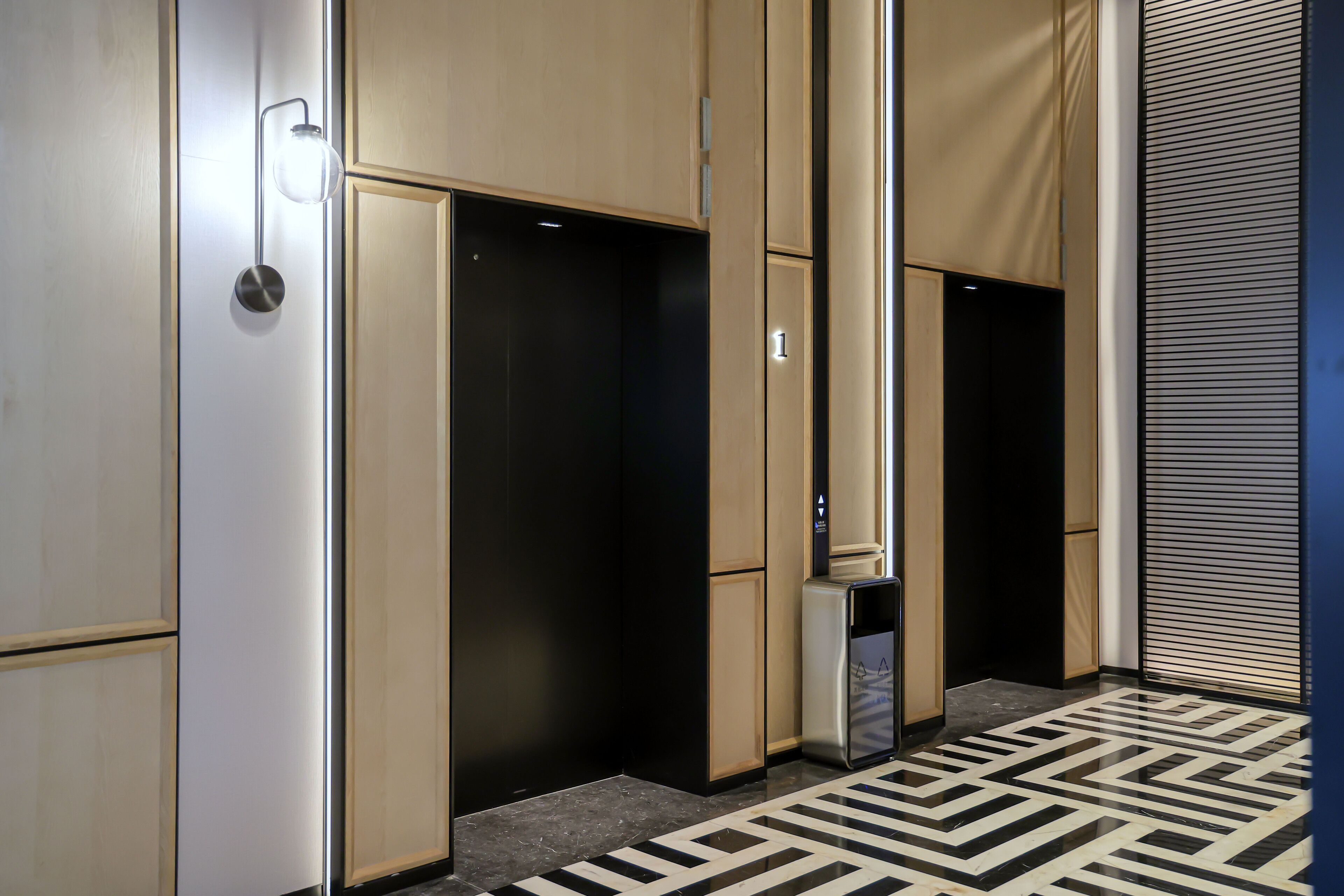 A hallway with a patterned floor, a trash bin, and a door with a number.