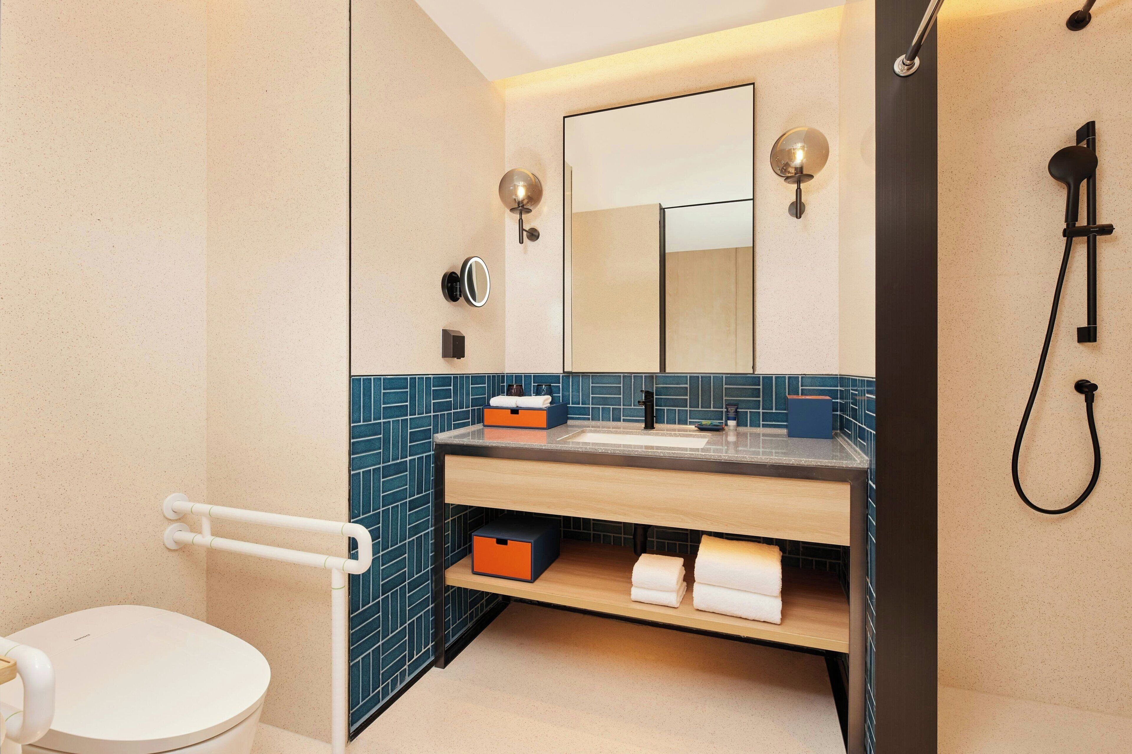 Un baño moderno con inodoro blanco, lavamanos con espejo y zona de ducha.