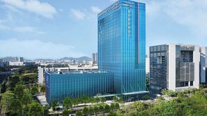 Ein modernes Hochhaus-Hotel mit einer markanten Glasfassade, umgeben von Grünflächen und weiteren Gebäuden.