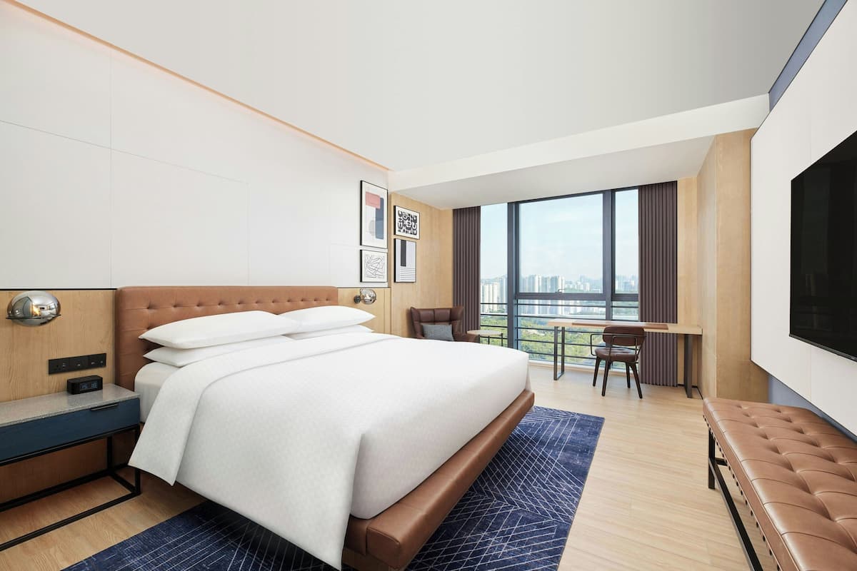 A modern hotel room with a large bed, a desk, a chair, and a TV.