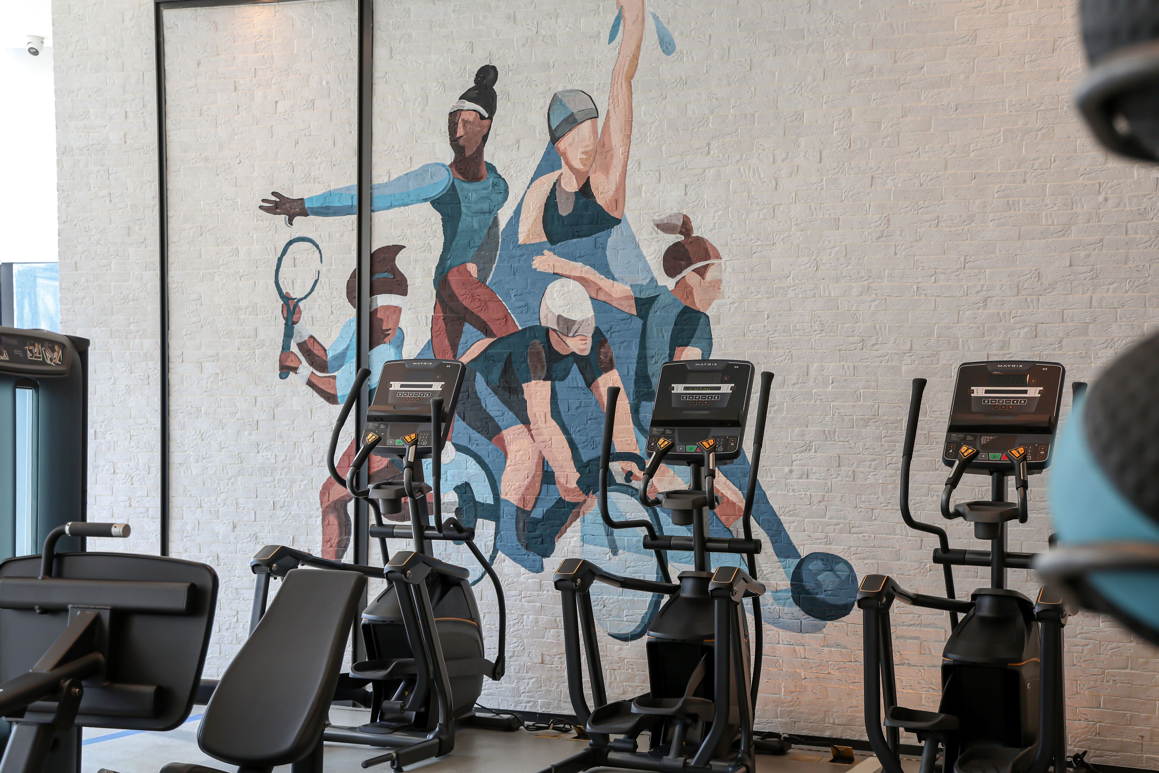 A gym with exercise equipment and a mural on the wall.