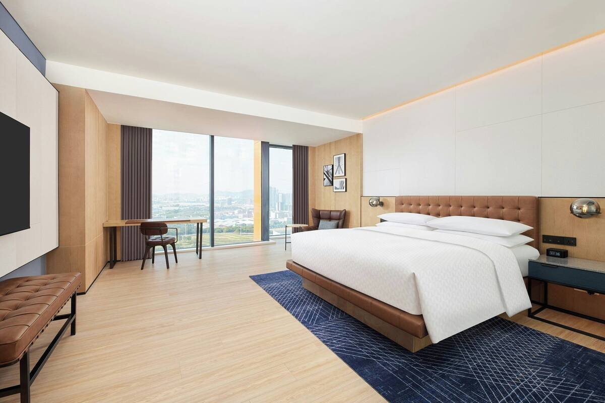 A modern hotel room with a large bed, a desk, a chair, and a view of the city.