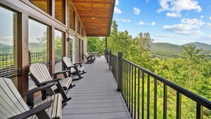 A wooden deck with outdoor seating and a view of a forested landscape. - Smoky Mountains Bliss - Cozy Cabin w/ Amazing Views, Perfect for Big Families!  (Sevierville)