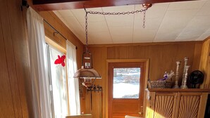 A wooden dining room with a table and chairs, a hanging light fixture, and a view of the outdoors through a window.