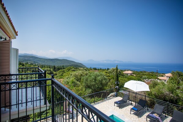 Un balcon avec une piscine, des chaises longues et une vue sur la mer et les montagnes.